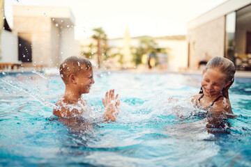 In a sunlit modern villa, a young brother and sister joyfully splash and play in the pool, basking in the warmth of a perfect summer day