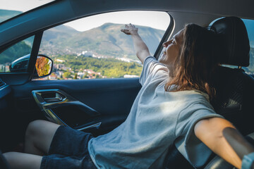A young woman enjoying a car trip in the passenger seat. Vacations and summer travel concept - obrazy, fototapety, plakaty