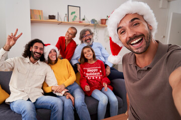 Happy family christmas selfie in the living room, everyone looking at camera smiling, celebrating together the day. Copy space.