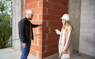 Woman standing by brick wall and discussing apartment replanning and renovation with specialist....