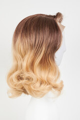 Naklejka premium Natural looking blonde fair wig on white mannequin head. Middle length hair cut on the plastic wig holder isolated on white background, side view.