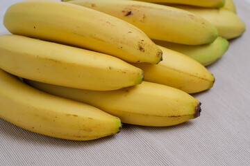 Close up of bunch of organic banana fruits isolated on white background. Barely ripe yellow bananas on beige linen fabric on the table in the kitchen.