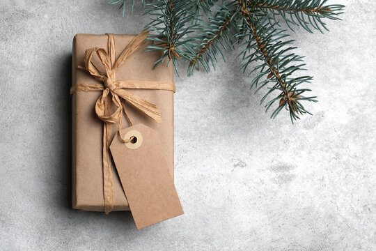 Christmas holidays box with craft gift tag and fir tree branch on grey background, top view, mockup with copy space