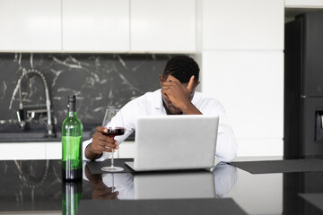 Black businessman depressed stressed from life problems and business fail drink alcohol front laptop computer alone at home - 659916743