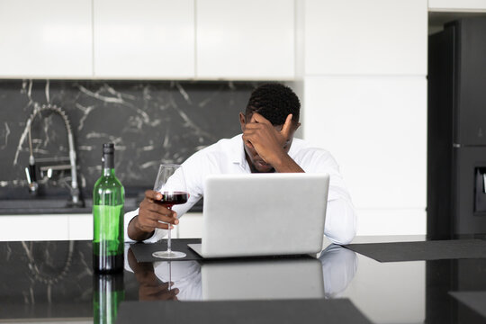 Black businessman depressed stressed from life problems and business fail drink alcohol front laptop computer alone at home
