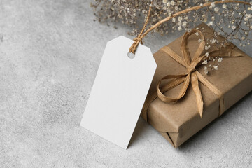 White price tag or label with gift box and dry gypsophila flowers on grey concrete background