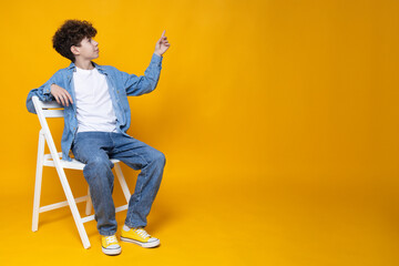 Attractive teenage guy on a chair, on a yellow background.