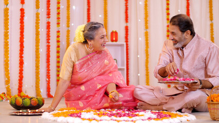 An old-aged Indian couple is decorating a floral Rangoli with rose petals for Diwali. An Indian...