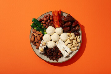 Plate with nuts and sweets on orange background, top view