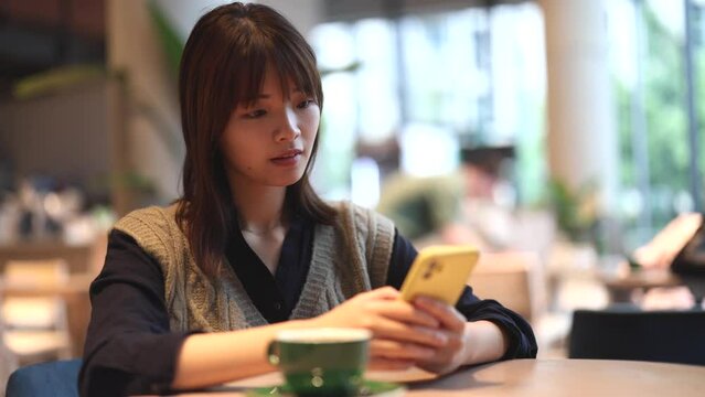 Asian woman in a coffee shop drinking coffee and looking at her smartphone
