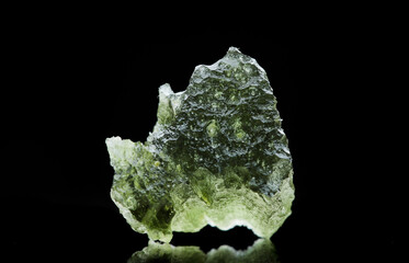 Moldavite stone isolated on black background. Close up macrophotograph of a green precious mineral...