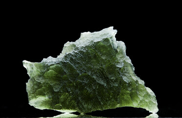 Moldavite stone isolated on black background. Close up of a green precious Czech gemstone. Genuine natural tektite glass.