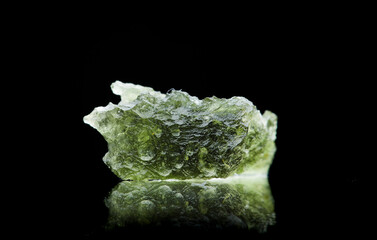 Moldavite stone isolated on black background. Close up macrophotograph of a green precious mineral...