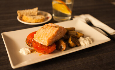 Steamed salmon fillet on a pillow of fried mushrooms and tomatoes on a white plate