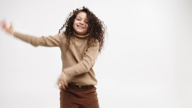Smiling child dancing on a light background, smiling little girl dancing, having fun to the music. The concept of a cheerful and carefree childhood