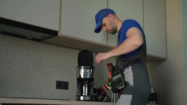 Repairman with screwdriver fixing coffee machine at indoors.