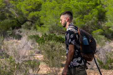 Fototapeta na wymiar Caucasian man with a backpack and canteen walking in the mountains. Side view photo