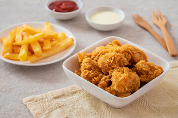 Crispy popcorn chicken in bowl with french fries on plate and sauce.