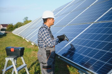 Male arabian engineer in helmet and brown overalls checking resistance in solar panels outdoors. Indian man working on station