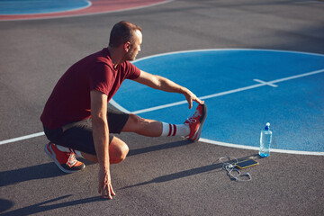 Man exercising and stretching on a public basket court in an urban park.