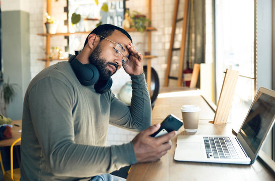 Man, Phone And Stress In Coffee Shop For Remote Work, Job Search Or Bad News Of Financial Fail, Debt Or Loan. African Freelancer With Headache, Worry Or Reading On Mobile, Business Decision And Cafe