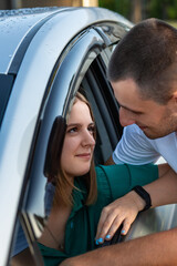 Fototapeta premium Young pretty caucasian couple kissing through an opened window of their car laughing and having fun together