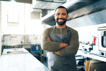 Happy man, chef and small business owner in kitchen at restaurant for hospitality service, cooking or food. Portrait of male person, employee or waiter smile in confidence for professional culinary