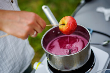 Dipping candy apple into glass bowl with caramel.