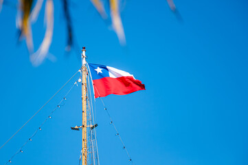Flag of the Republic of Chile, on top of a  mast waving with blue sky as background.