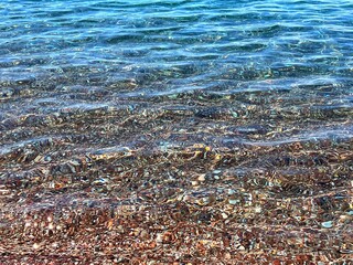 Sea waves blue transparent colorful pebbles stones sand at the bottom.