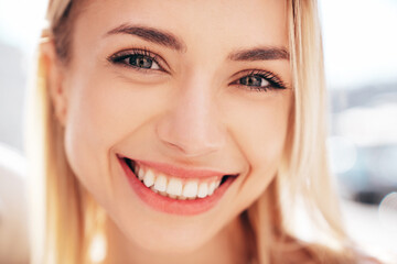 Closeup portrait of young beautiful smiling woman in trendy. Sexy carefree model posing on the street background at sunset. Positive blond female. Cheerful and happy
