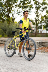 Fototapeta premium Dorosły mężczyzna z protezą ręki w stroju sportowym jedzie, pchając rower górski ręką. Koncepcja niepełnosprawnych kolarzy. Sportowcy z niepełnosprawnością.