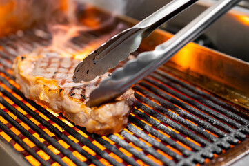 cooking beef steak on grill in restaurant kitchen