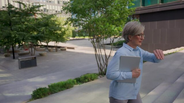 Caucasian old senior woman walking up stairs outdoors female lady businesswoman lawyer run with folder documents hurry walk climbing steps stairway of office building late for business meeting in city