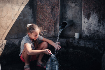 cute caucasian girl draws clean water at the bottle from a spring in the forest at the autumn day
