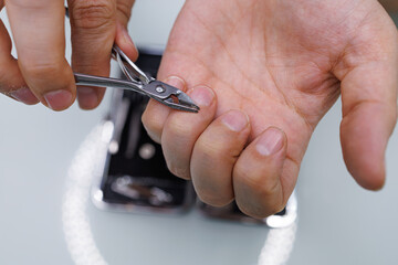 Men's hands cut off the excess skin near the nail with professional clippers. A man gives himself a manicure