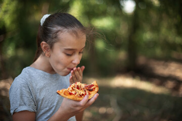 hungry cute caucasian girl eats a piece of pizza with appetite in the forest on a summer day