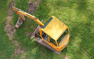 Fototapeta premium Small digger excavator, parked on green grass, aerial view from above