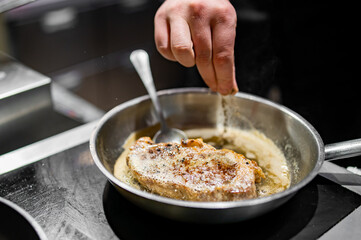 Professional chef cooking beef steak in frying pan on stove in restaurant kitchen