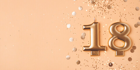 Gold candles in the form of number eighteen on peach background with confetti. 18 years...
