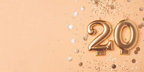 Gold candles in the form of number twenty on peach background with confetti. 20 years anniversary celebration.