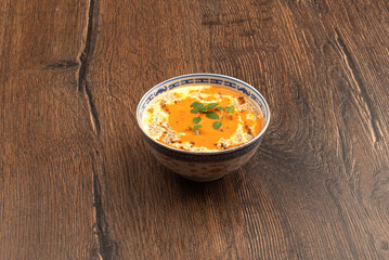 Bowl with tomato puree soup with cream and green basil leaves on a wooden background.