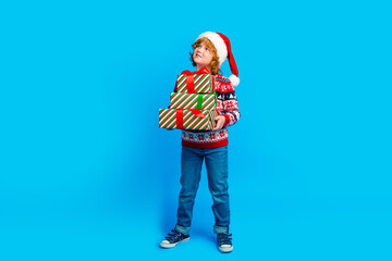 Full length photo of cute dreamy little boy dressed ugly pullover x-mas hat holding gifts empty space isolated blue color background