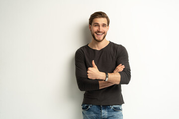 Portrait of cheerful man in casual clothing smiling and showing thumbs up at camera isolated over...