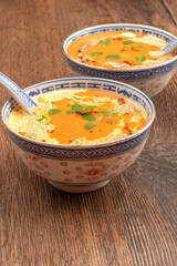 Close-up of autumn tomato puree soup with cream and green basil leaves.