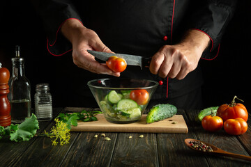 The cook adds tomato to a fresh vegetable salad in the kitchen. Knife in the hand of the chef. Healthy vegetarian food concept