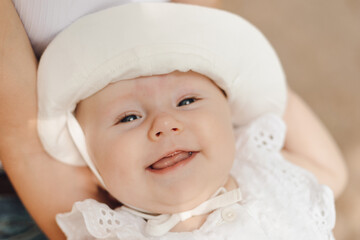 Close-up portrait of smiling toothless newborn girl in hat, held in arms of unrecognizable mother. 