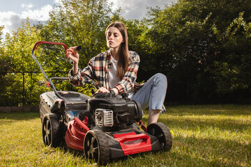 Female gardener working in autumn, cutting grass in backyard. Concept of gardening, work, nature. Housework, gardening and country life. Home garden grass cutting woman mowing with lawn mower.

