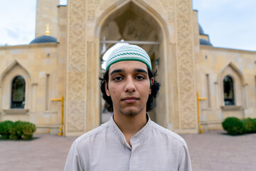 portrait of a young man of Muslim appearance leaving the mosque after prayer on terrace with Islamic ornaments 