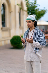 Fototapeta na wymiar A guy of Arab appearance in national clothes with rosary around his neck prays in the courtyard of the mosque